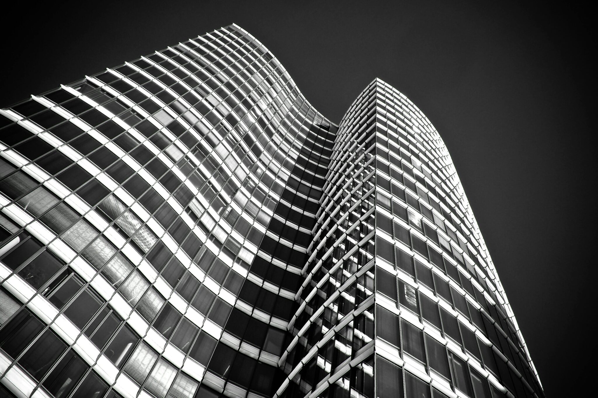 Low angle view of a futuristic skyscraper with glass facades and steel structure in black and white.